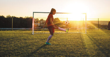 girl kicking soccer ball at dusk