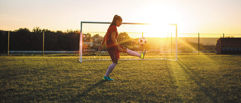 girl kicking soccer ball at dusk