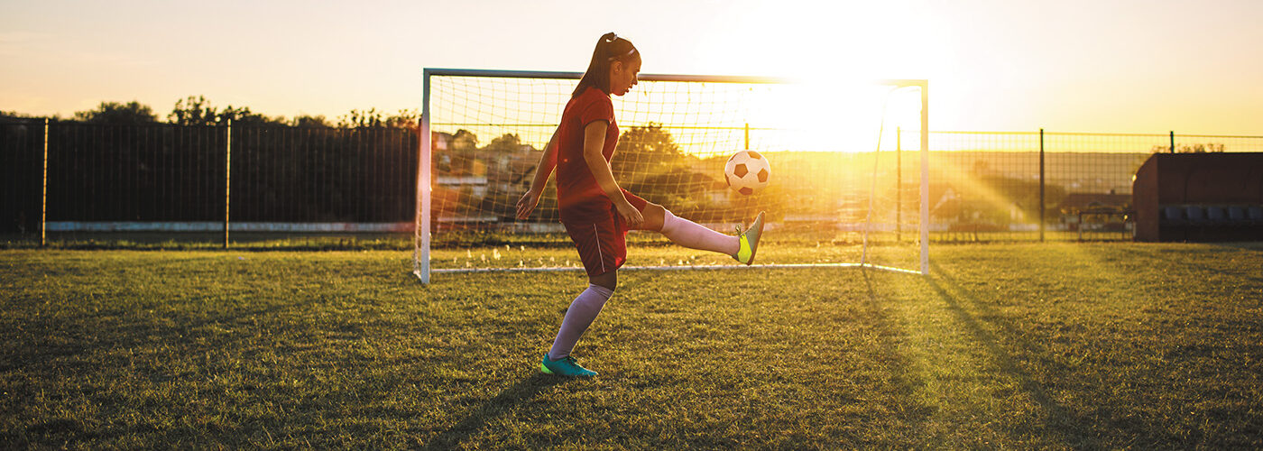 girl kicking soccer ball at dusk