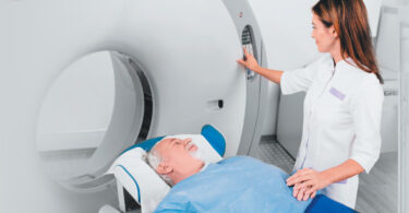 Female nurse holds hand of male patient as he lays on MRI machine