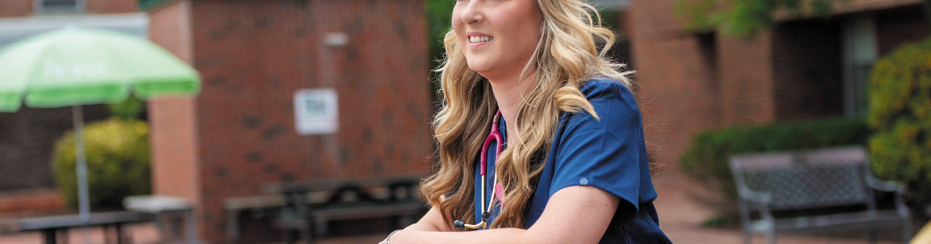 Female nurse in front of a building smiling and staring far off.