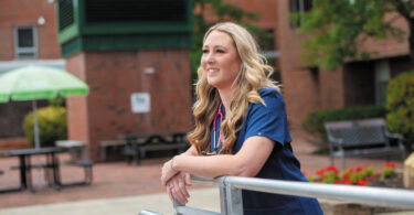 Female nurse in front of a building smiling and staring far off.