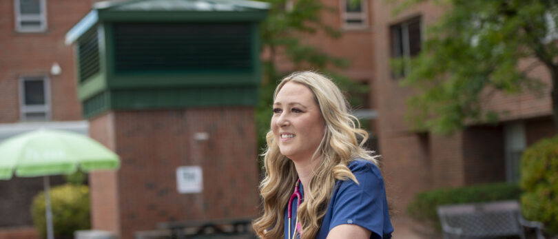 Female nurse in front of a building smiling and staring far off.