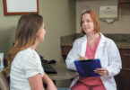 Female doctor holding a clipboard talking to a patient.