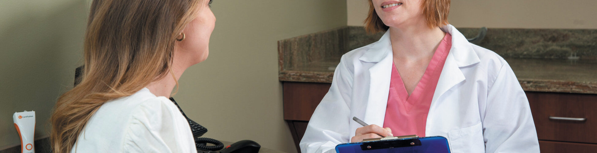 Female doctor holding a clipboard talking to a patient.