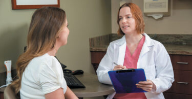 Female doctor holding a clipboard talking to a patient.