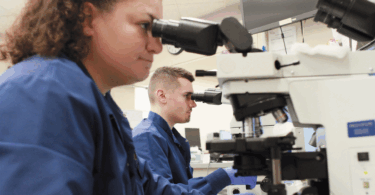 Two lab technicians looking at samples through a machine.