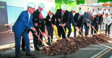 Men and women in construction hats and suits breaking ground at the new UHS Upper Front Street facility.