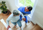 A home health worker helps an elderly woman walk up the stairs.