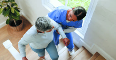 A home health worker helps an elderly woman walk up the stairs.