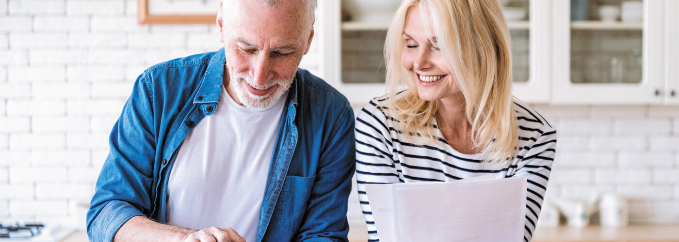 An older couple looking at a paper bill and phone smiling.