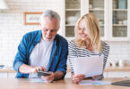 An older couple looking at a paper bill and phone smiling.