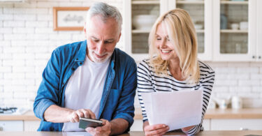 An older couple looking at a paper bill and phone smiling.