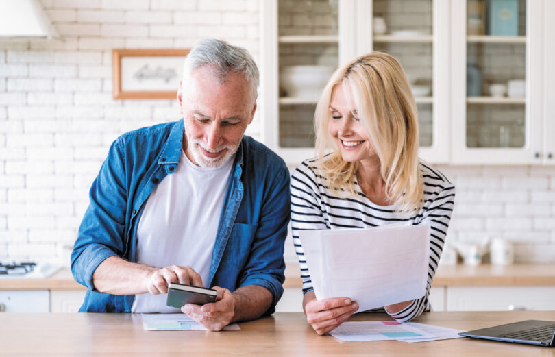 An older couple looking at a paper bill and phone smiling.